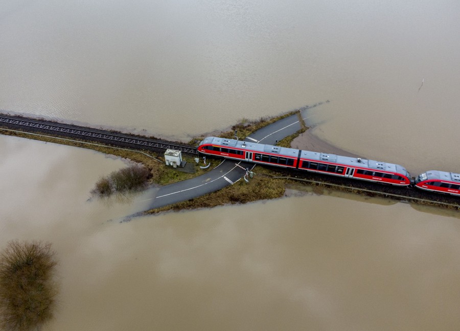A train crosses a road on a small high patch of land among floodwaters.