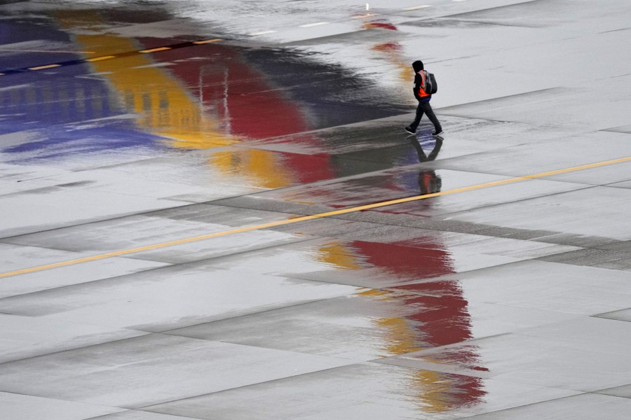 A person walks near an airplane, which is reflected in wet pavement.