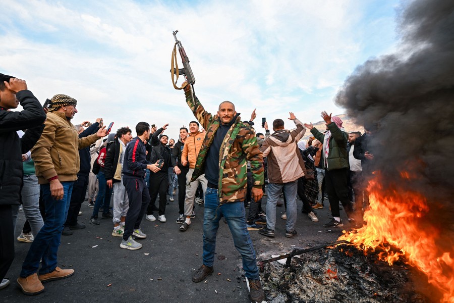 A crowd celebrates beside a bonfire. One man holds a rifle above his head.