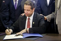 Andrew Cuomo signs a bill. There are six other pens he does not appear to be using but that stand at the ready should the ink run dry.