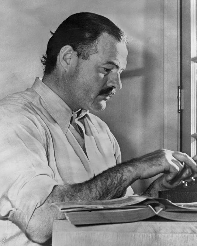 A black-and-white photo of Ernest Hemingway working at a typewriter