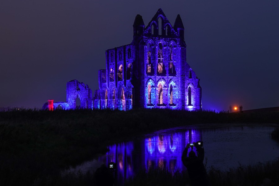 The ruins of an old abbey are illuminated with colorful lights at night.