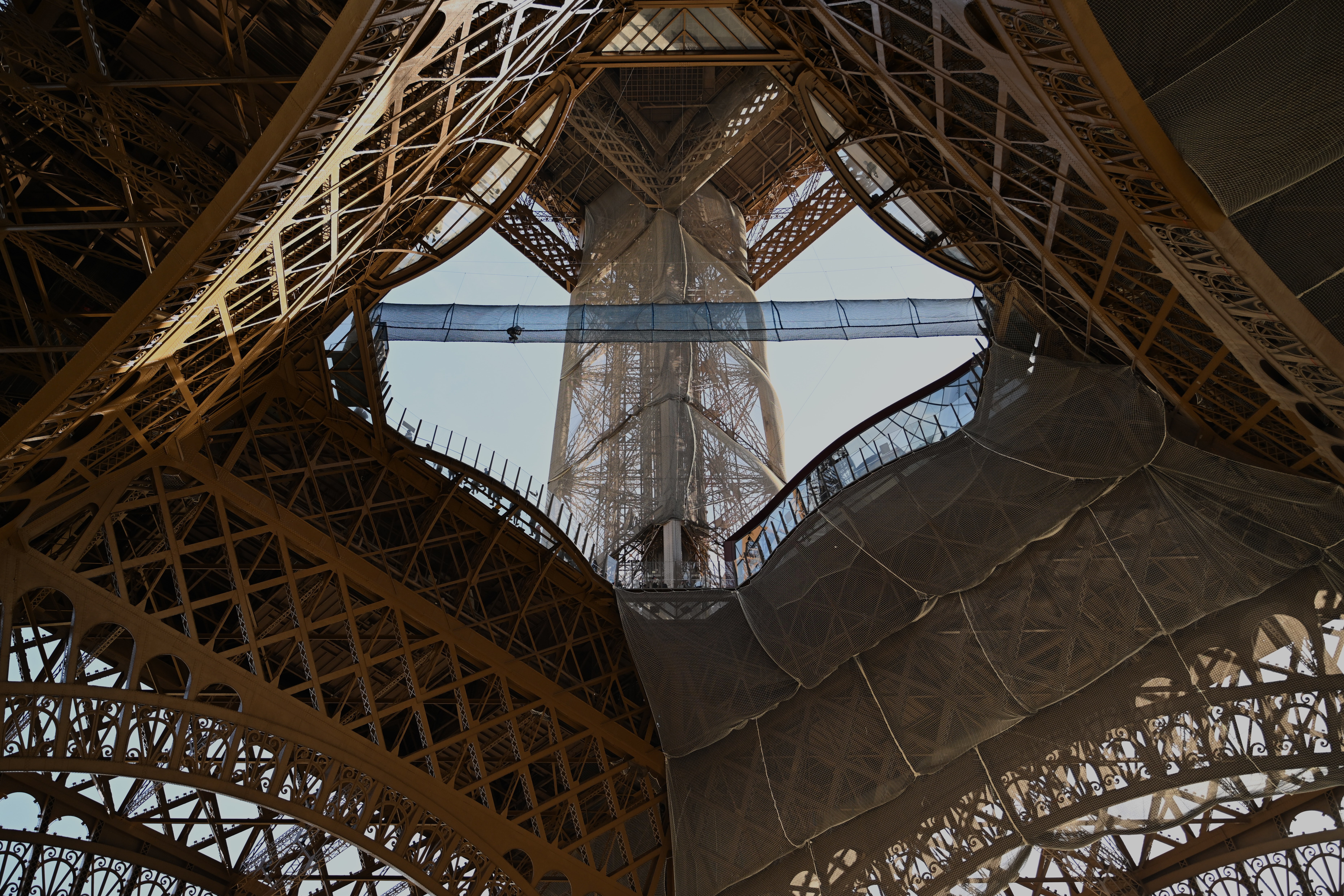 A person crosses a bridge made of rope and netting, inside the Eiffel Tower.