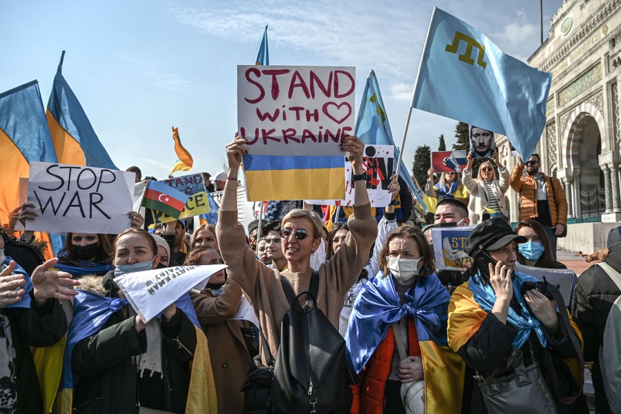 Protest marchers carry Ukrainian flags and handwritten signs, one of which reads "Stand with Ukraine."