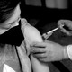 A young person wearing a mask receives a shot in the arm