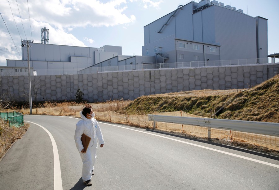 A woman in a protective suit walks on a road beside a large industrial building.