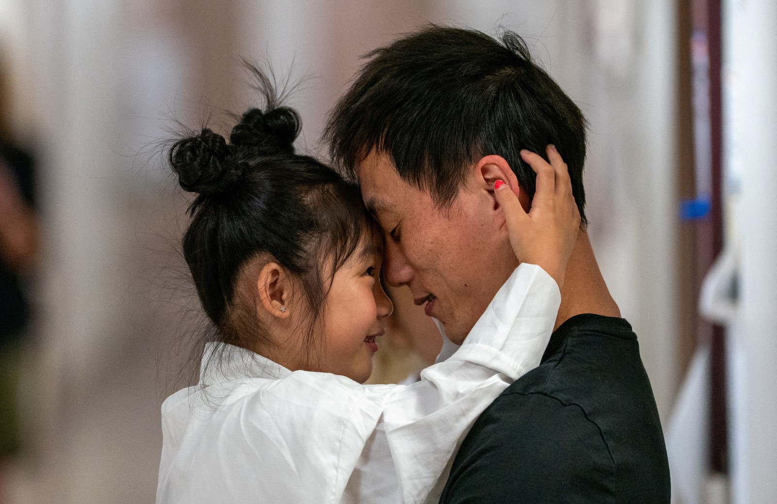 A child hugs their father, the two of them pressing their foreheads together and smiling.