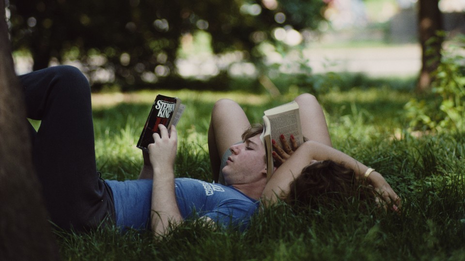 Two people lay in the grass and read books