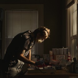 A medic leans over a desk in a darkened room, preparing medical supplies.