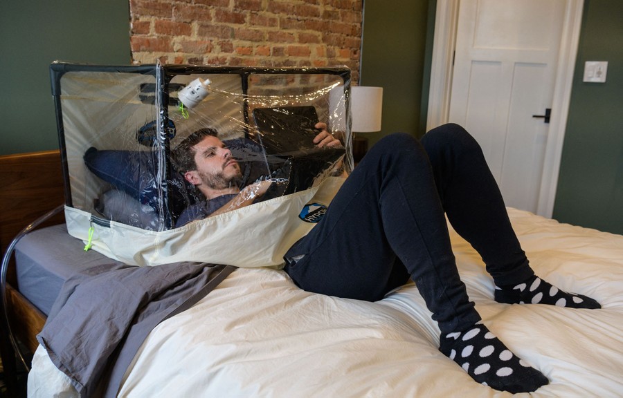 A man lies in bed, with his upper half inside a clear plastic tent.