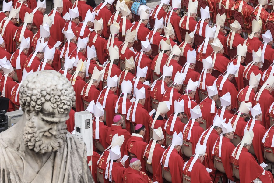 Dozens of red-robed cardinals sit in rows.
