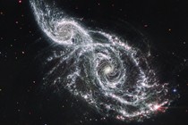 Two spiral galaxies take up almost the entire view and appear to be overlapping. The background of space is black, dotted with tiny foreground stars and extremely distant galaxies.