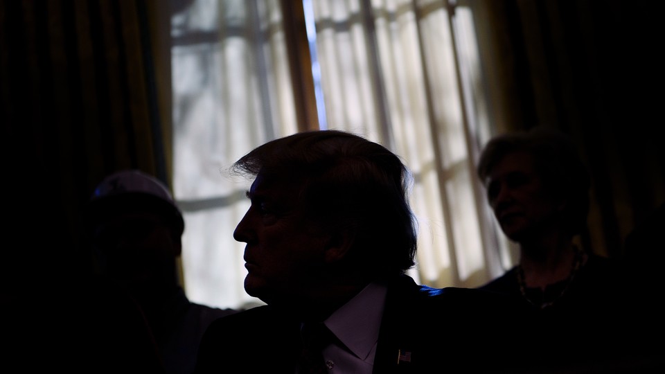 Trump sits in front of a window with his face obscured by shadows.