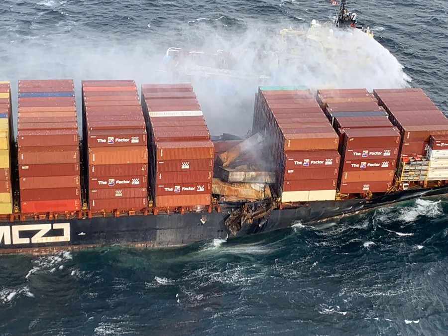 Water is sprayed onto a container ship carrying damaged and smoldering containers.