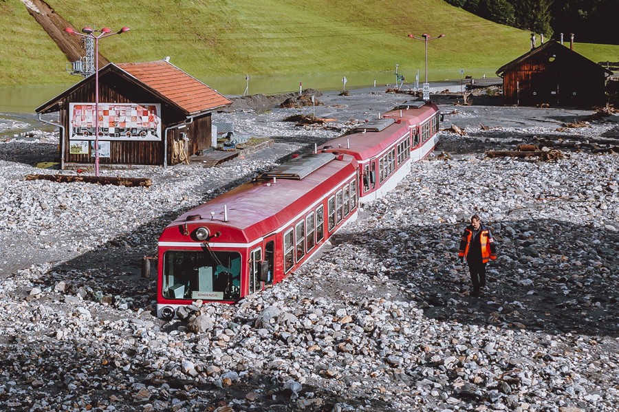 A three-car passenger train is partially buried in mud and rocks in a narrow valley.