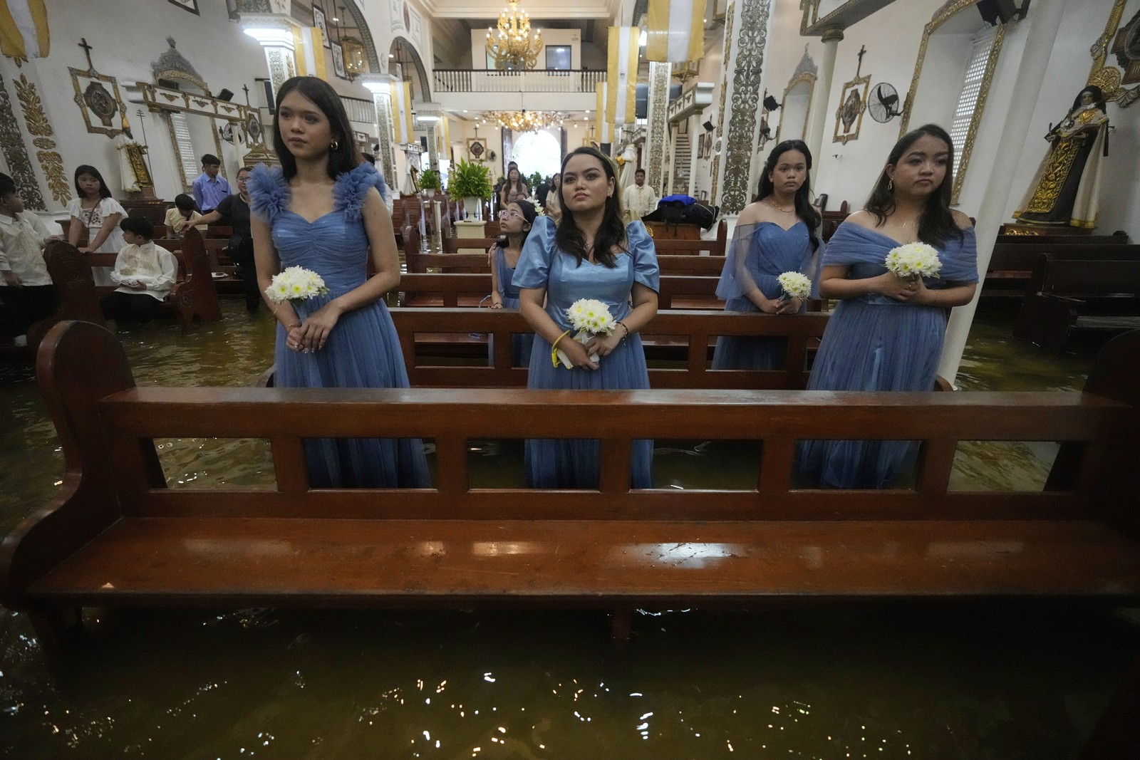 Five bridesmaids stand and sit among the pews in a flooded church.