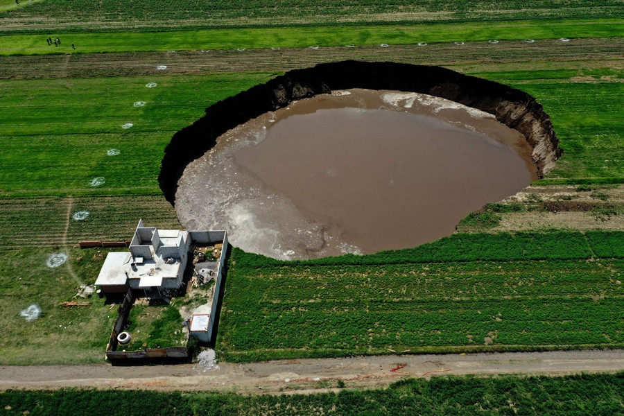 A large sinkhole is seen in a field alongside a house.