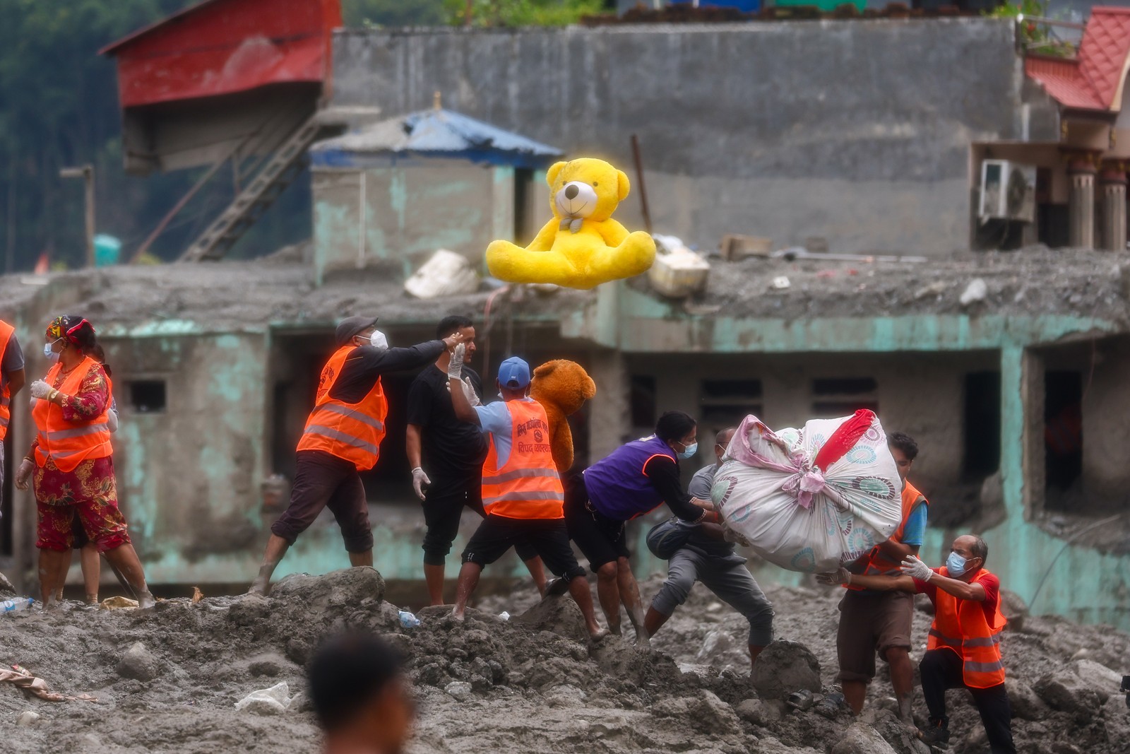 Workers transfer belongings, including a large yellow teddy bear, from flood-damaged homes.