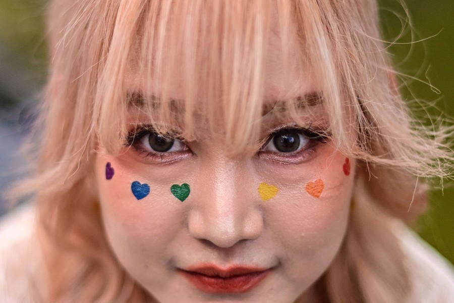 A person poses for a photo, with multicolored hearts painted on their cheeks.