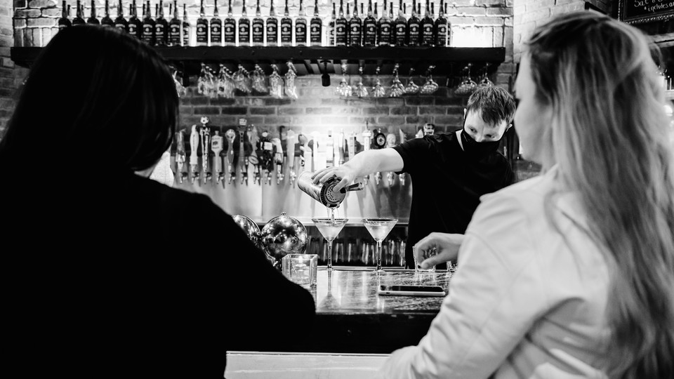 Two women sitting at a bar while a bartender pours a drink