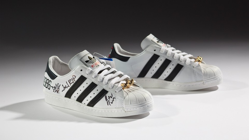 A pair of white sneakers with black Adidas stripes on the side and a handwritten signature.