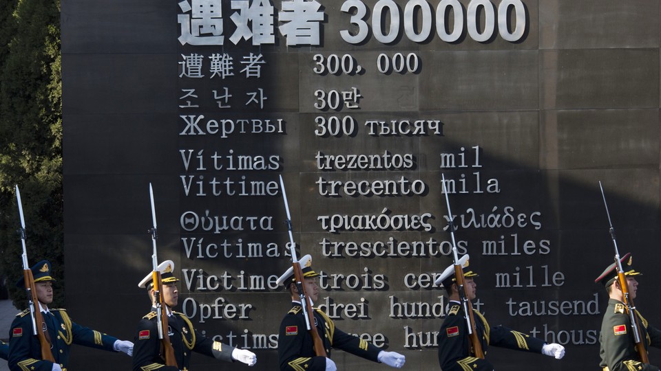 Chinese honor guard members march past the words "Victims 300000."
