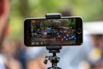 A person uses an iPhone on a tripod to broadcast an event to Facebook Live.