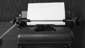 A black-and-white photograph of a Remington typewriter with a blank sheet of paper set up