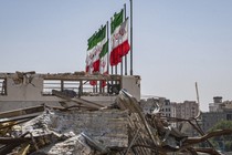 A color photo of Iranian flags flying above a bomb-damaged building.