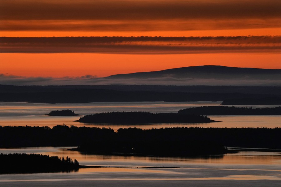 Many bays and inlets around a collection of forested islands are colored by a reddish predawn sky.