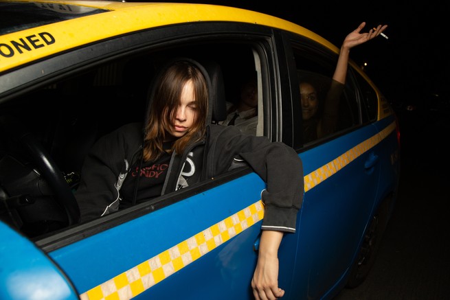 a young woman driving a taxi with a friend in back