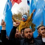 A boy in a blue mask raises two East Turkestan flags in a march.