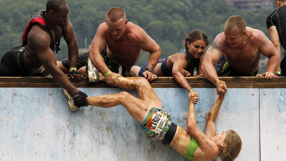 Athletes pull a mud-covered team member over a wall