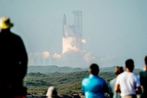 Spectators look on as the Starship rocket lifts off in a blaze in the distance
