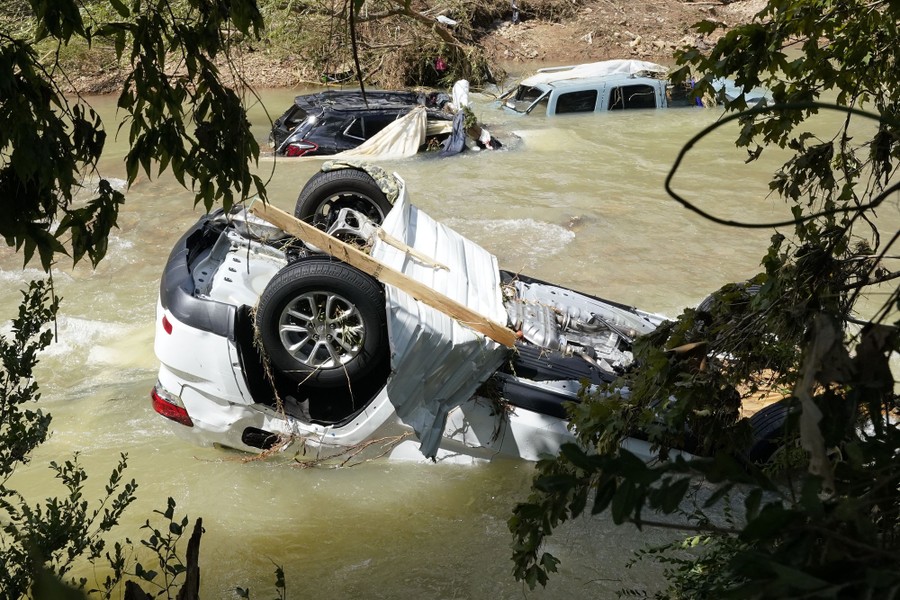 Several cars and trucks sit partially submerged in a stream.