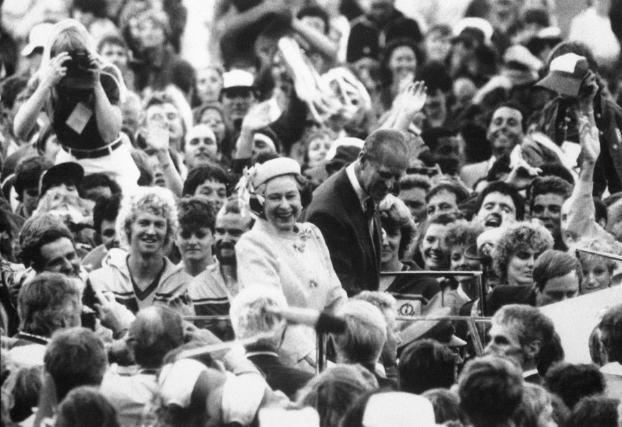 The Queen and her husband are surrounded by a large crowd of fans.
