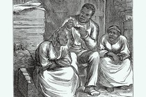 A man reads a Bible to two women in what looks like a barn.
