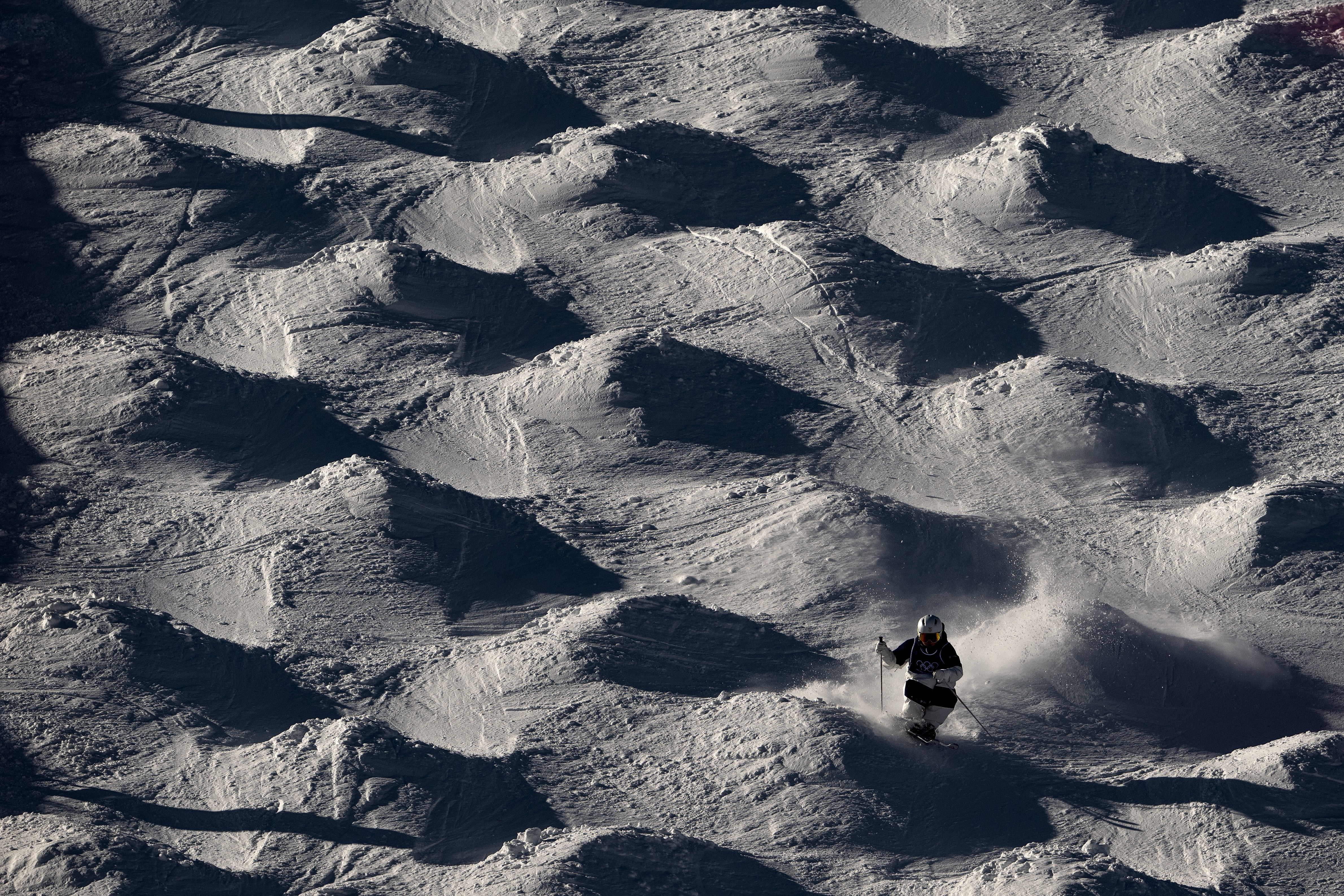 A high-contrast view of a skier navigating undulating moguls on a ski slope.