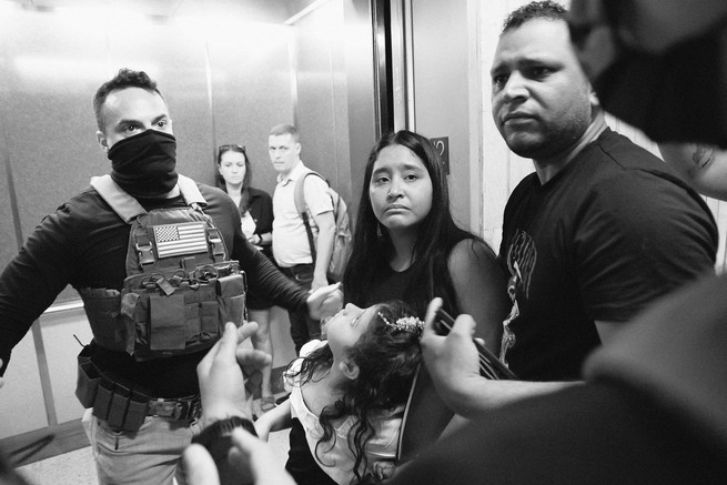 a black and white photo of ICE officers detaining a family at an immigration hearing.