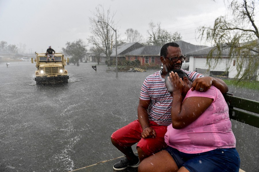 People being evacuated in the back of a tall truck are soaked by a sudden rain shower.