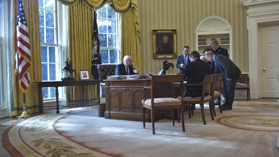 President Donald Trump speaks on the phone from the Oval Office as staffers look on.