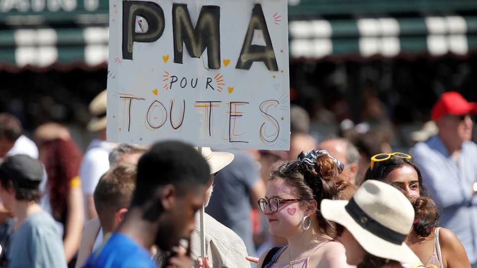 A participant in the Paris gay pride parade holds up a placard which reads "PMA (Fertility treatment) for all."