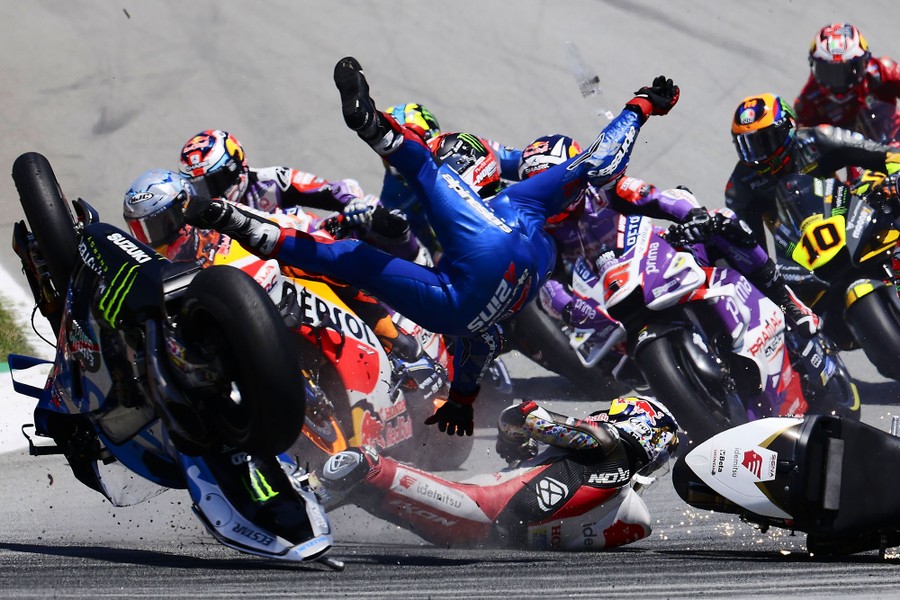 Two motorcycle riders tumble after a crash, as other racers speed past.