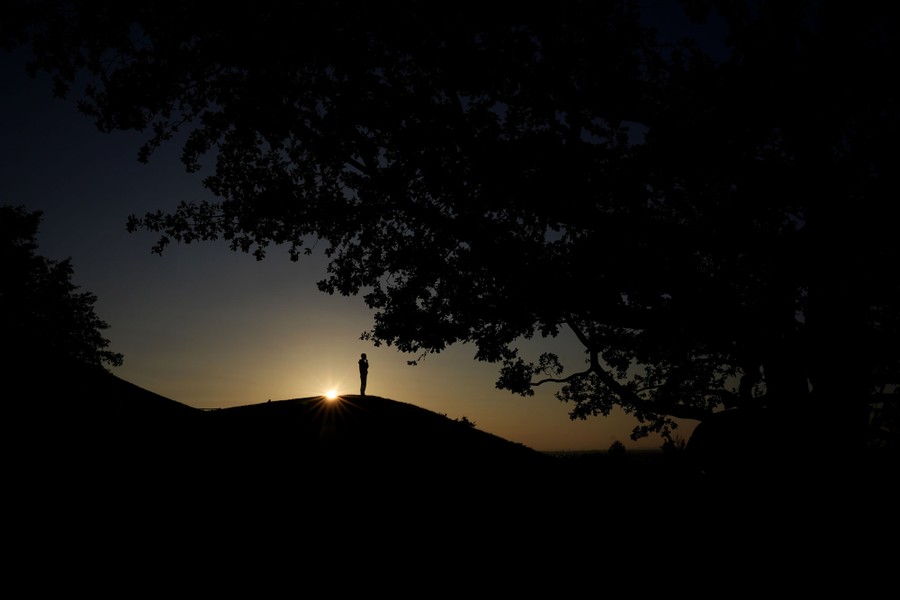A man is silhouetted on a hill as the sun sets.