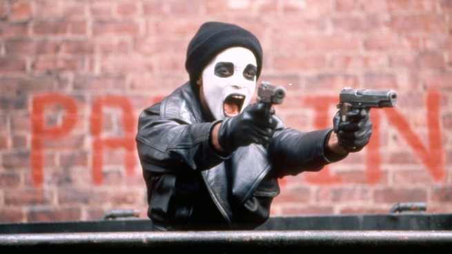 A man in a face mask holds two guns, from the movie "Dead Presidents."