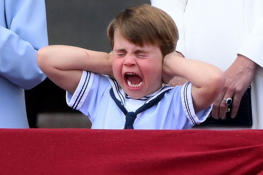 A young boy yells while holding his hands over his ears.