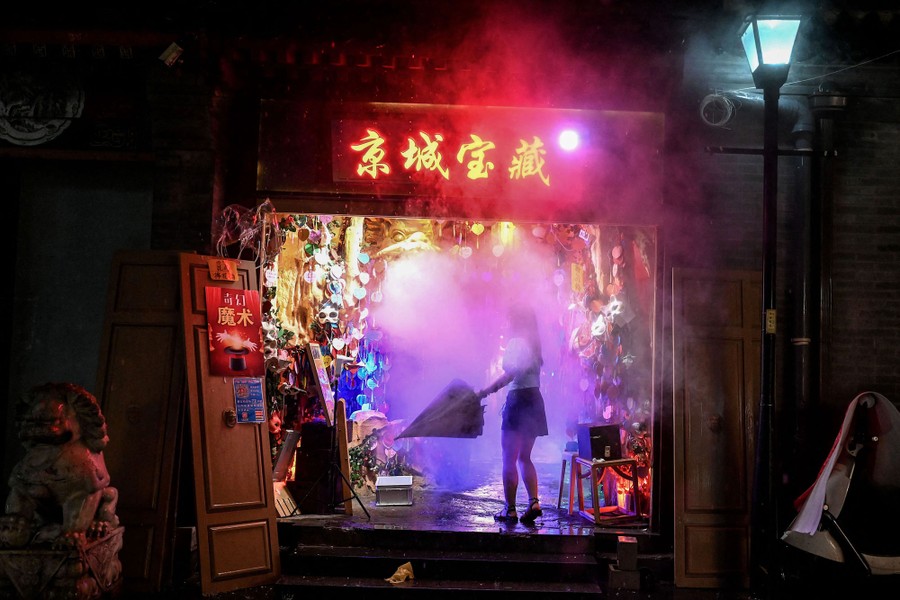 A woman folds an umbrella in the misty entrance to a gift shop at night.