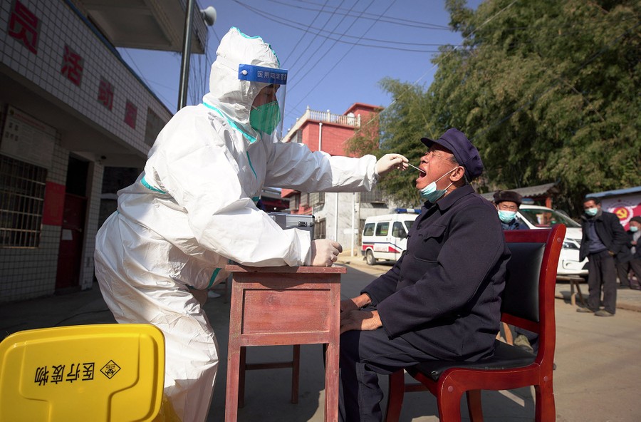 A health worker wearing protective gear takes a swab sample from a man's mouth.