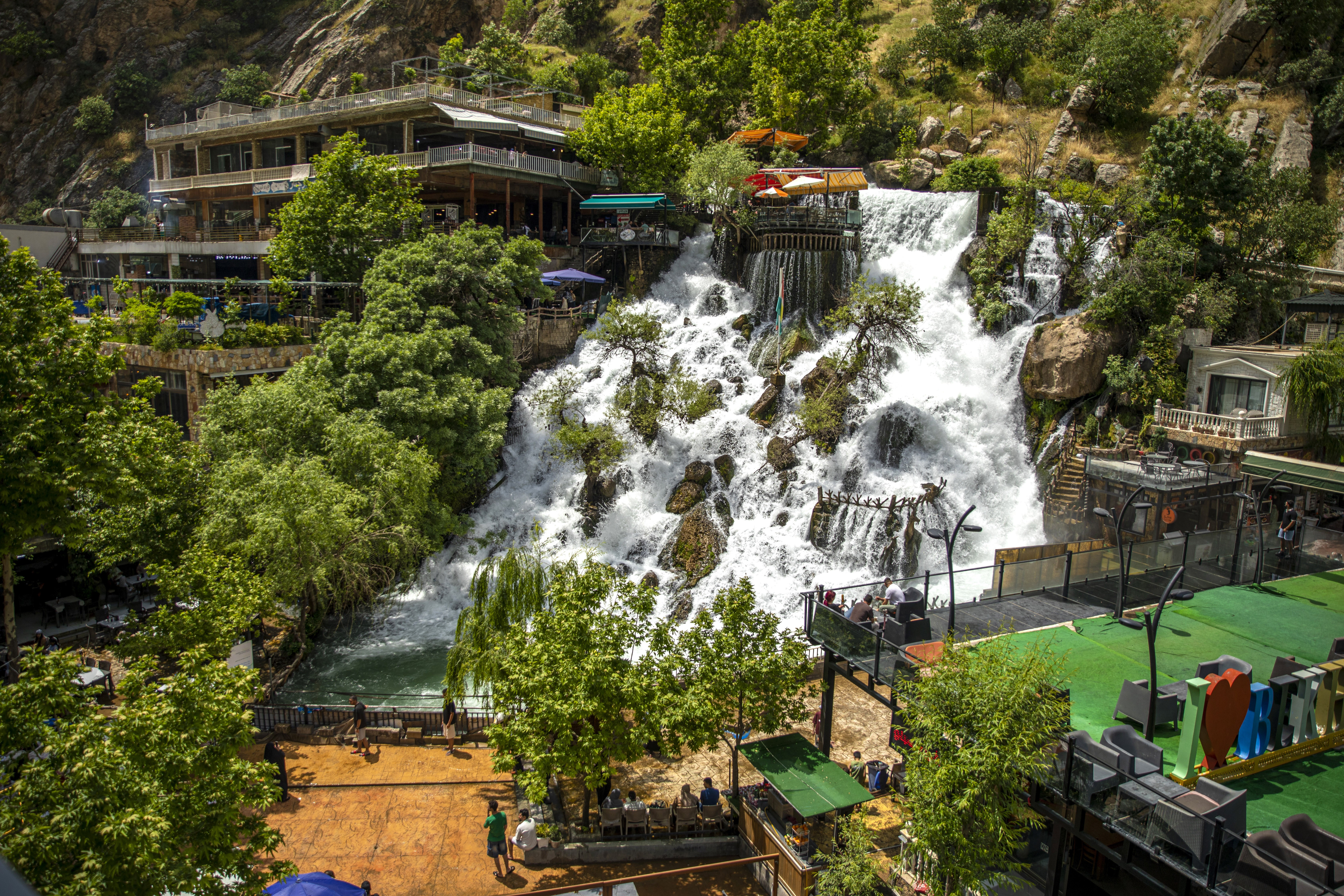 People view a broad waterfall flowing past buildings and observation decks.