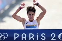 An athlete reacts as they reach the finish line of a race, raising their arms up to grab at the ribbon across the line.